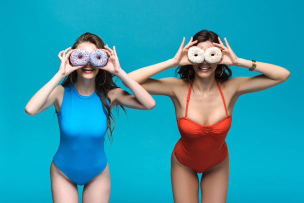 two girls in swimsuits holding donuts isolated on blue - Foto, Imagem