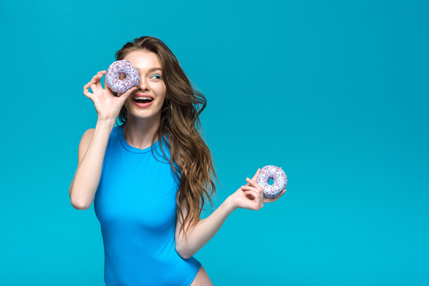 smiling girl in swimsuit holding donuts isolated on blue - Photo, Image