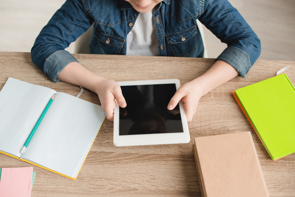 cropped view of boy holding digital tablet with blank screen while sitting at desk with notebooks - Photo, Image