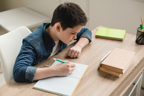 vista de ángulo alto de niño atento escribiendo en el libro de copia mientras que hace el trabajo escolar en casa
 - Foto, imagen