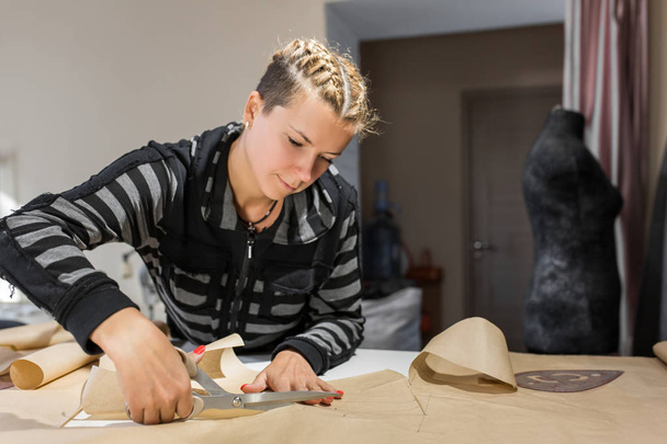 Blonde woman seamstress cuts from craft paper pattern for making - Фото, зображення