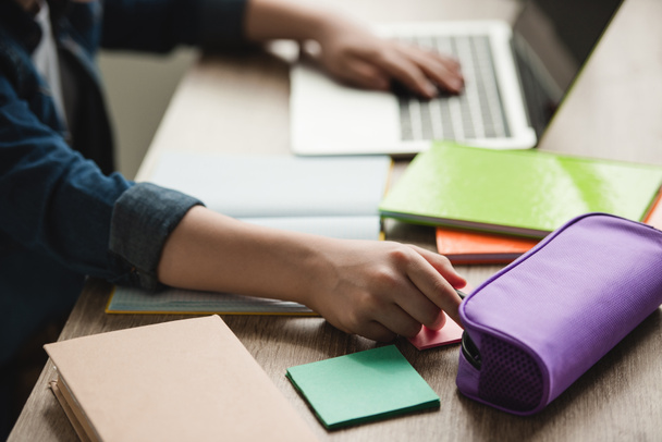 обрізаний вид школяра за допомогою ноутбука, сидячи за столом з копіювальними книгами і роблячи домашнє завдання
 - Фото, зображення