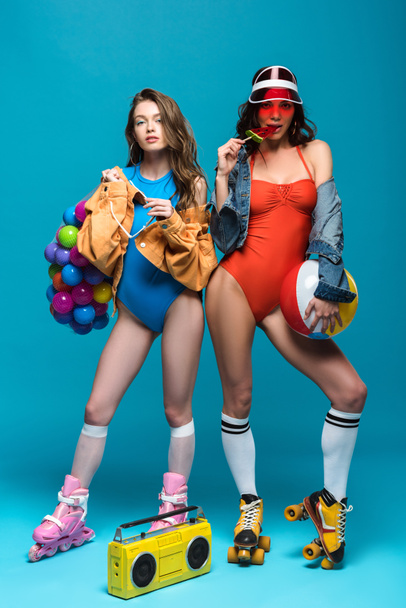 full length view of two stylish girls in roller skates eating watermelon lollipop on blue - Фото, зображення