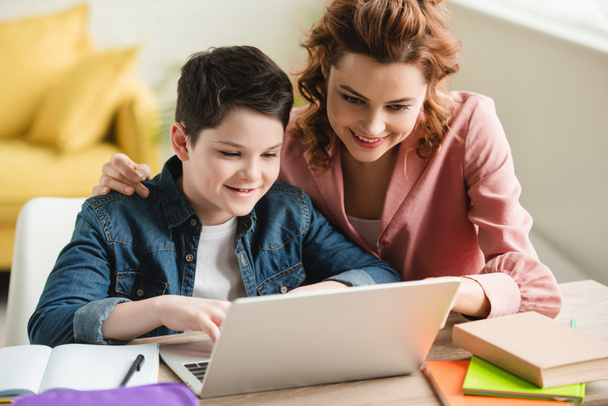 happy mother embracing adorable son while using laptop together  - Photo, Image