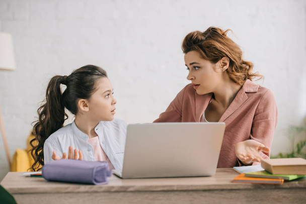 discouraged woman showing shrug gesture while using laptop together with daughter - Photo, Image