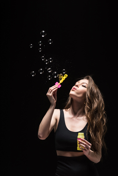 pretty young woman blowing soap bubbles isolated on black - Fotó, kép