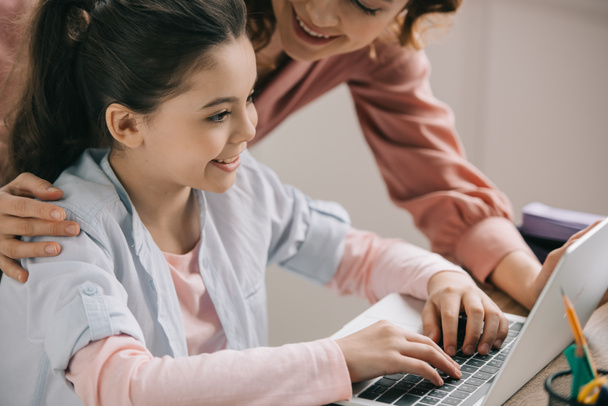 selective focus of smiling child using laptop near smiling mother - Фото, зображення