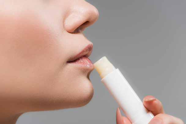 bijgesneden beeld van vrouw vasthouden lippenbalsem geïsoleerd op grijs  - Foto, afbeelding