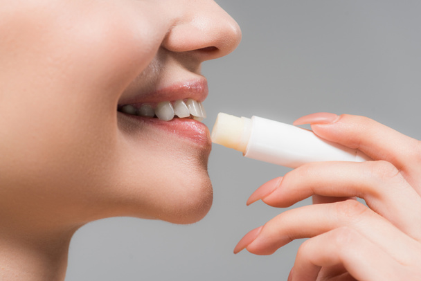 cropped view of cheerful girl holding lip balm near lips isolated on grey  - Photo, Image