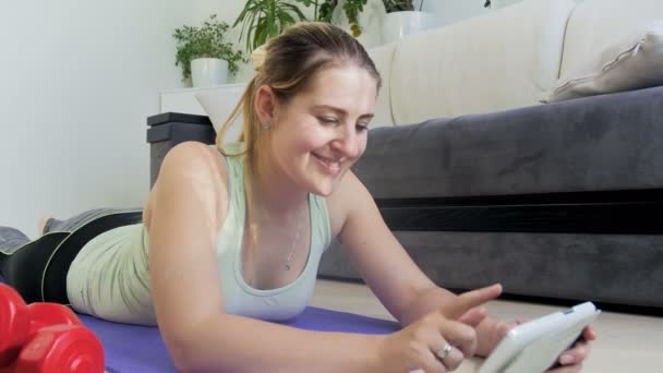 4k video of young woman exercising on floor a thome. She is watching how to do exercises oand stretching on tablet computer - Video, Çekim