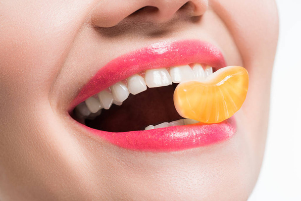 abgeschnittene Ansicht eines lächelnden Mädchens beim Essen von Orangengelee-Bonbons isoliert auf Weiß  - Foto, Bild