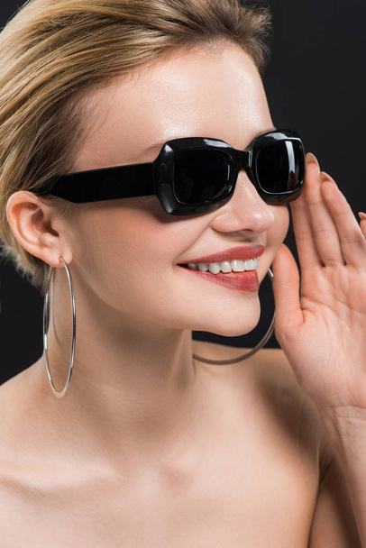 glückliche Frau mit Sonnenbrille lächelt vereinzelt auf schwarz  - Foto, Bild