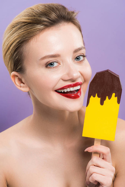 веселая женщина держит картонное мороженое и улыбается изолированы на фиолетовый
  - Фото, изображение