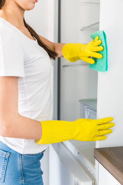 Egy fiatal nő egy profi takarítócégtől otthon takarít. Egy férfi lemossa a konyhát, sárga kesztyűben mossa a hűtőt tisztítószerekkel.. - Fotó, kép