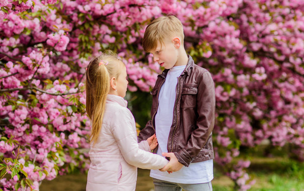 Romantic date in park. Spring time to fall in love. Kids in love pink cherry blossom. Love is in the air. Couple adorable lovely kids walk sakura garden. Tender love feelings. Little girl and boy - Photo, Image