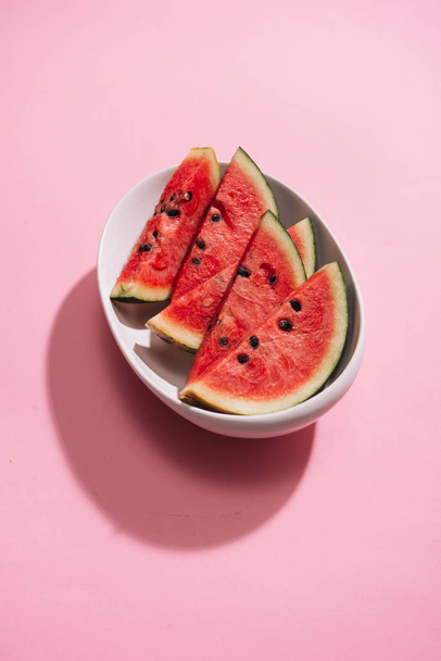 Fresh sliced watermelon in white dish on pink background. - Photo, Image