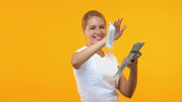 Extremely happy woman throwing dollars against orange background, lottery winner - Filmati, video