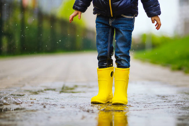 nogi dziecka z żółtymi gumowymi butami wskoczyć w kałuży na jesiennym spacerze - Zdjęcie, obraz