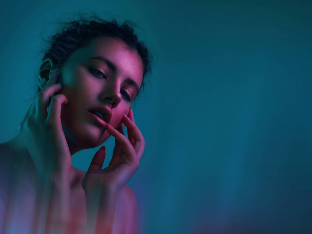 Modetrend Nahaufnahme Porträt eines jungen Mädchens in bunten hellen Neonlichtern posiert im Studio. Mädchen Glanz Gesicht in blauer und lila Farbe Licht auf dunkelblauem Hintergrund - Foto, Bild