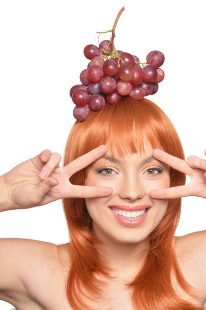 Portrait of beautiful redhead young woman with red grapes on head showing peace signs isolated on white background - Foto, Imagen