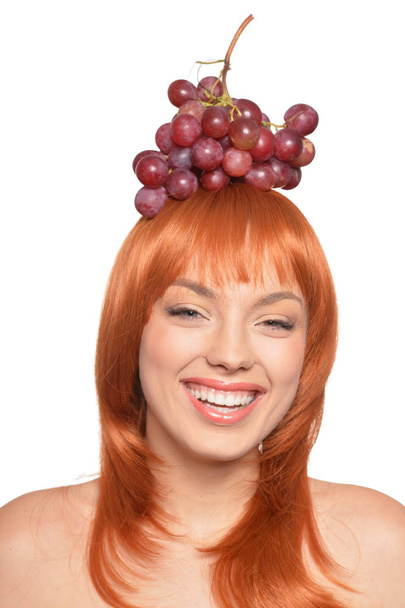 Portrait of beautiful redhead young woman with red grapes on head isolated on white background - Фото, зображення