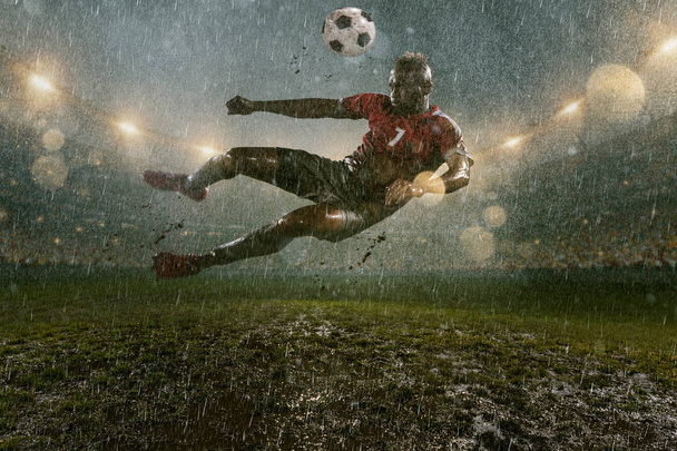 Soccer players performs an action play on a professional night rain stadium. Dirty players in rain drops scores a goal. Grass in the stadium wet from the rain - Photo, Image