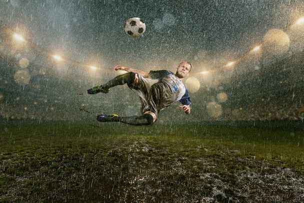 Piłkarzy wykonuje akcję gry na profesjonalnym stadionie nocnym deszczu. Brudnych graczy w deszczu krople strzeli gola. Trawa na stadionie mokra od deszczu - Zdjęcie, obraz