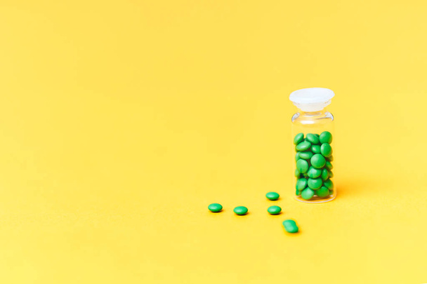 Medische groene pillen in een glazen fles op gele achtergrond copyspace, gezondheid - Foto, afbeelding