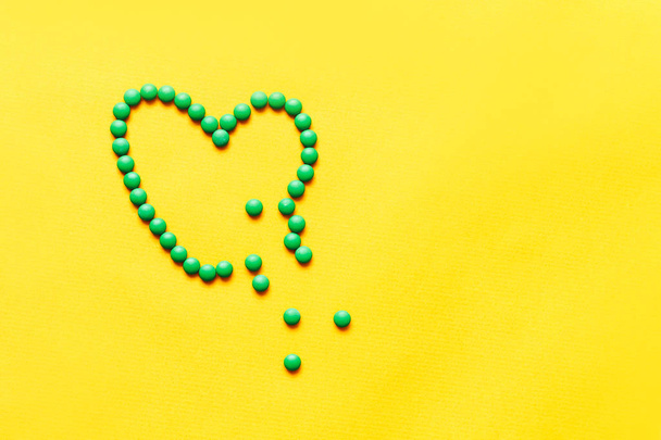 pastillas redondas verdes comprimidos brocken forma de corazón sobre fondo amarillento
 - Foto, Imagen
