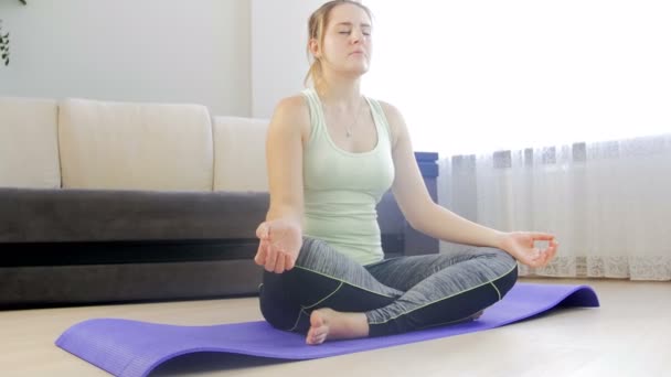Dolly 4k images de belle jeune femme assise position de yoga lotus sur tapis de fitness au salon et méditant
 - Séquence, vidéo