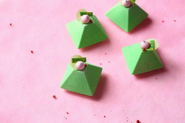 Piramide-hedendaagse groene thee Matcha mini mousse cake met aardbei Jelly, bedekt met groene fluwelen spray en versierd met roze meringue cookie, op licht roze achtergrond. - Foto, afbeelding