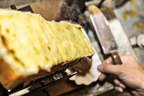 Raclette auf dem Raclette-Grill ist bereits gegrillt und mit einem Messer auf dem Brot ausgebreitet und es raucht schön - Foto, Bild