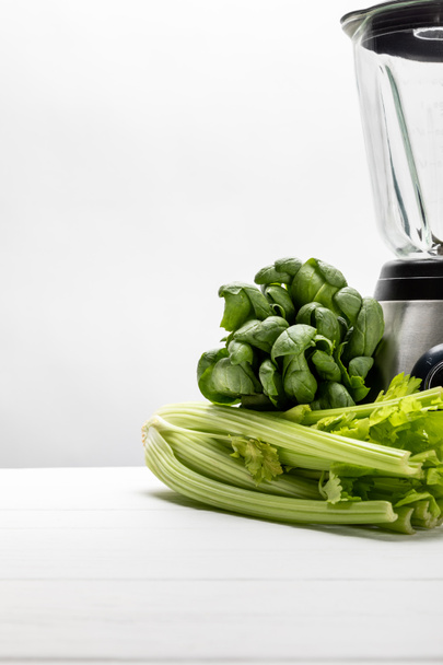 green fresh spinach leaves near organic celery and blender on white  - Photo, image
