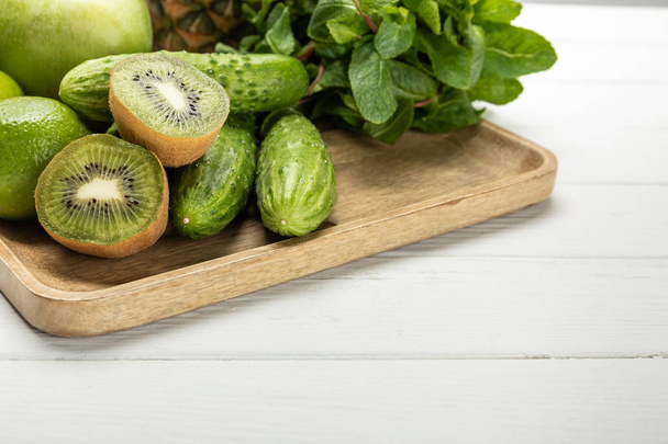 halves of tasty ripe kiwi fruit near cucumbers on wooden chopping board  - Photo, Image