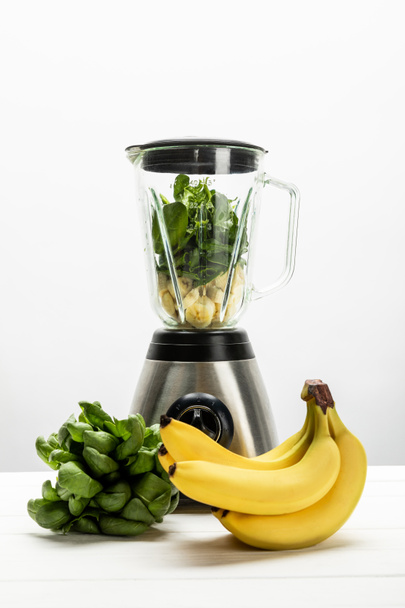 green spinach leaves and yellow ripe bananas near blender on white  - Foto, imagen