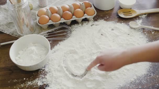 台所のテーブルで白い小麦粉の流出の碑文ケーキ。カップケーキのコンセプトを作る.ホームベーキング。白い小麦粉の背景に調理指書きの単語 - 映像、動画