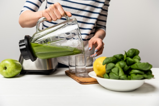 cropped view of woman pouring tasty green smoothie in glass near apple on grey  - Photo, Image