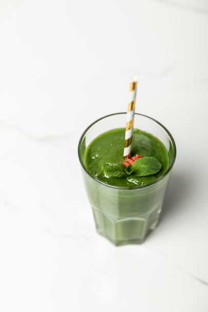 overhead view of green, organic smoothie with goji berries and mint in glass with straw on white  - Foto, imagen