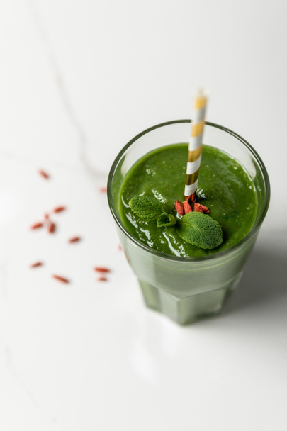 selective focus of green smoothie with goji berries and mint in glass with straw on white  - Foto, imagen