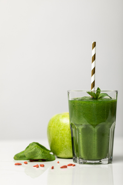 зелена смугаста в склянці з соломою біля стигле органічне яблуко на сірому
  - Фото, зображення