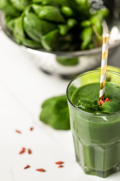 selective focus of tasty smoothie with goji berries and mint in glass with straw near spinach leaves on white  - Photo, Image