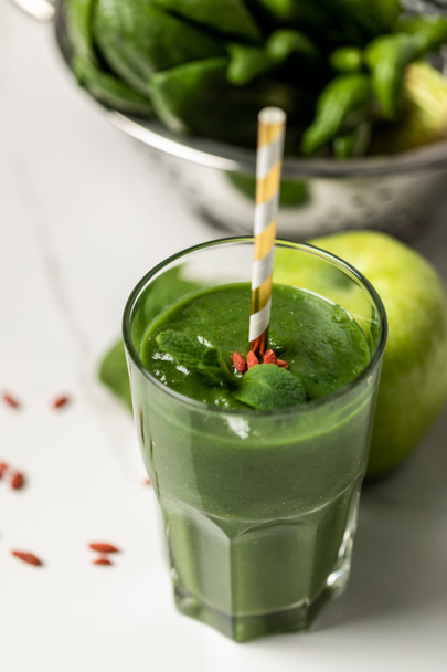selective focus of tasty smoothie in glass with straw near spinach leaves and apple on white  - Fotó, kép