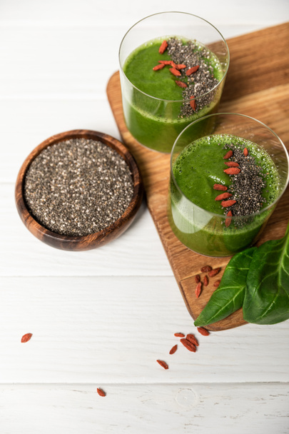 top view of chia seeds in bowl near glasses of green smoothie on white  - Fotografie, Obrázek
