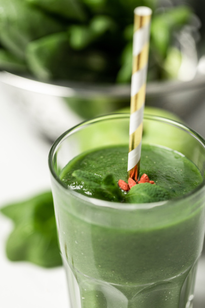 selective focus of tasty green smoothie in glass with straw near spinach leaves on white  - Фото, зображення