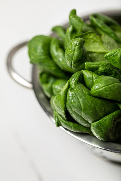 selective focus of green fresh and organic spinach leaves in colander on white - Foto, imagen