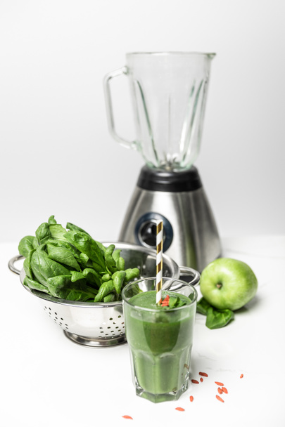 foco seletivo de smoothie verde em vidro com palha perto de folhas de espinafre fresco, maçã e liquidificador em branco
  - Foto, Imagem
