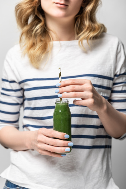 cropped view of woman holding straw and glass bottle with tasty green smoothie on white  - Foto, afbeelding