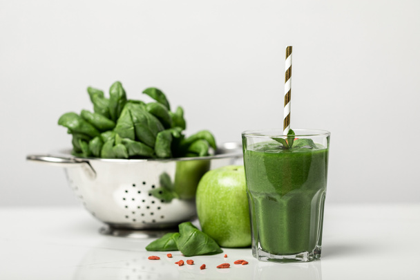 selective focus of green smoothie in glass with straw near spinach leaves and apple on white  - Photo, Image