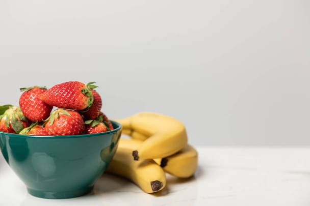 sweet and tasty strawberries in bowl near yellow bananas on grey  - 写真・画像