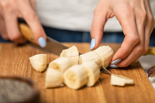 cropped view of woman cutting ripe and sweet bananas on cutting board  - Фото, зображення